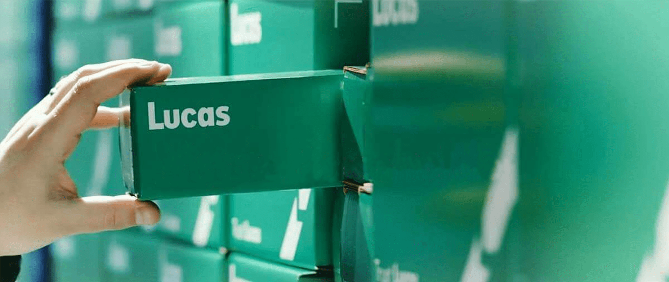 A hand pulls a green box labeled "Lucas" from a shelf filled with identical green boxes.