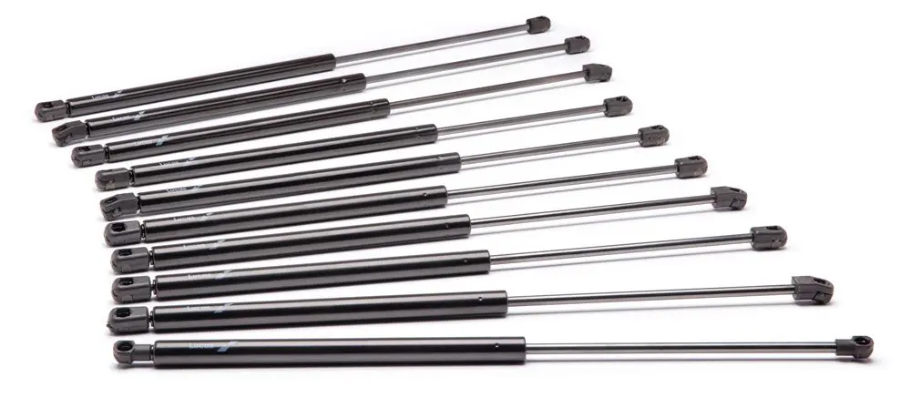 A row of eleven gas struts or gas springs with black cylindrical bodies, metal rods, and plastic mounting ends, arranged from shortest to longest.